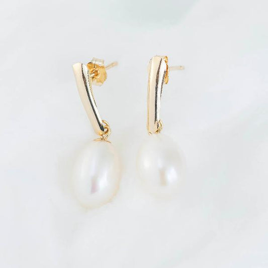 NY Gold & Silver Trading Inc.'s 14K Yellow Gold Freshwater Pearl Drop Earrings are an elegant, goddess-worthy piece with large white pearl drops against a soft white background.