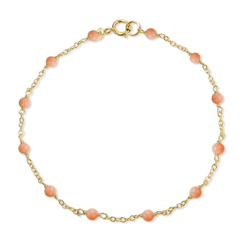 The 14k Pink Coral Station Bracelet from the Goddess Jewelry Collection is a delicate gold chain bracelet adorned with evenly spaced pink beads and a circular clasp, offering a subtle touch of color in its simple, elegant design.