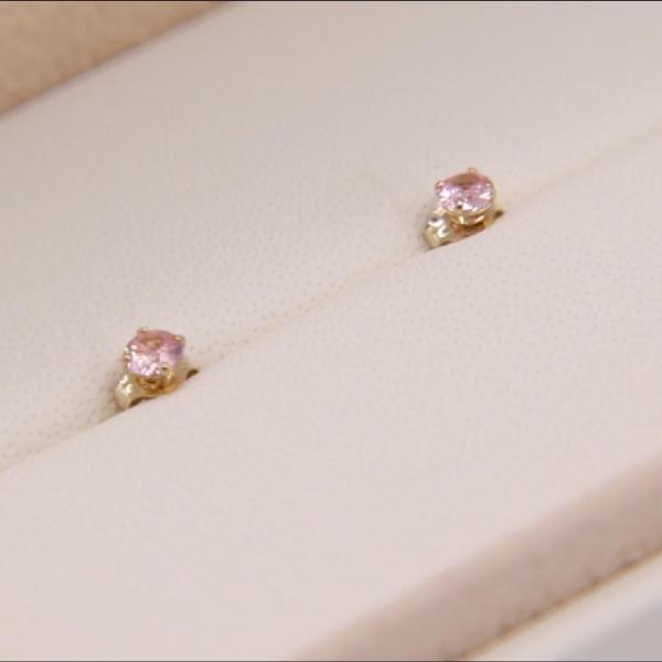 A pair of Tiny 14K Tourmaline 3mm Stud Earrings  from the Goddess Jewelry Collection , featuring small pink gems set in yellow gold, displayed in a cream-colored jewelry box.