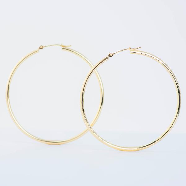 Two 14k Yellow Large Gold Hoop Earrings 2mm from the Goddess Jewelry Collection on a plain white background. Polished for luminous reflection, one hoop is positioned slightly in front of the other, forming a sense of depth.