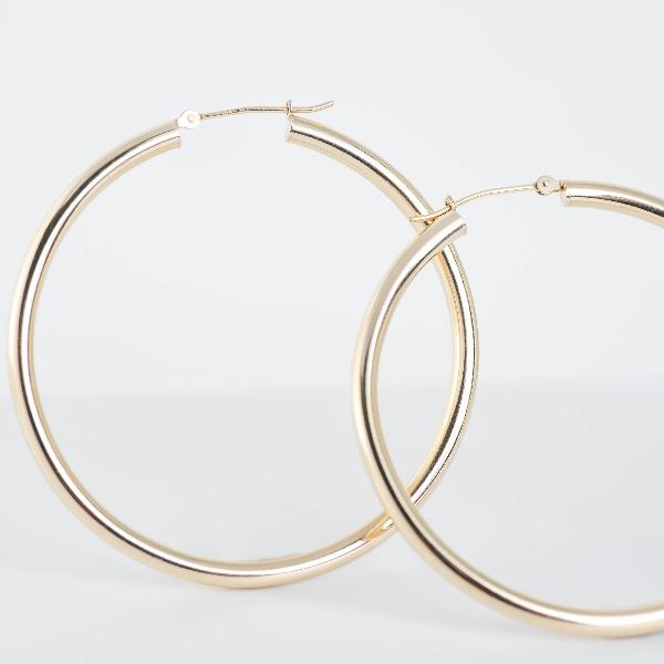 Two 14k Yellow Large Gold Hoop Earrings (3mm) from the Goddess Jewelry Collection sit on a plain white background, showcasing a simple, smooth finish with thin fastenings, exuding elegance and grace.
