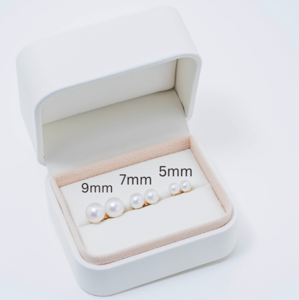 An open Jewelmak box reveals six pairs of 14k white freshwater pearl stud earrings, elegantly arranged in a size gradient from 9mm to 5mm. The box features a pristine white exterior and a soft beige interior, perfectly complementing the timeless beauty within.