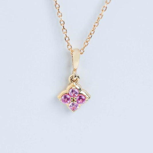 Stuller's Youth 14K Lab-Grown Pink Sapphire Necklace, with a flower-shaped pendant featuring lab-grown pink sapphires in a cross pattern and a delicate chain, stands elegantly against a light blue background.