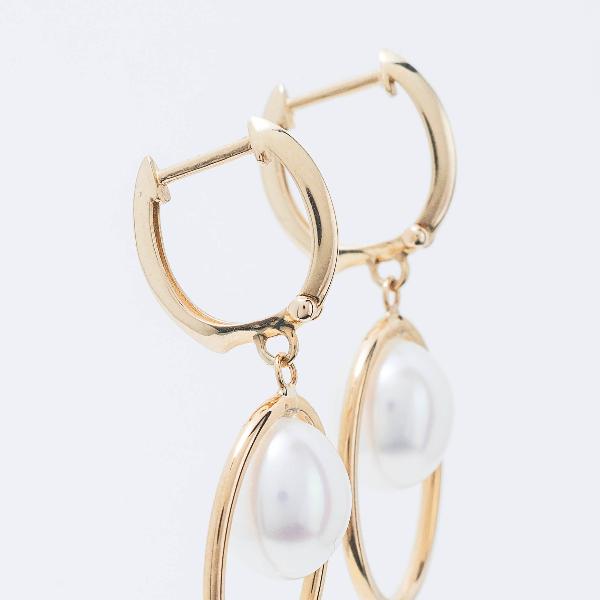 Set against a light gray background, 14k Freshwater White Pearl Huggie Hoop Earrings feature dangling white pearls framed by slim gold oval shapes, creating an elegant and sophisticated design.