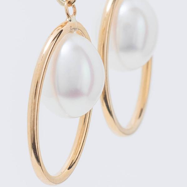 Close-up of 14k White Pearl Huggie Hoop Earrings featuring large freshwater pearls encircled by thin hoops, set against a plain light background.