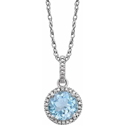 The Sterling Silver Natural Blue Topaz Round Necklace  from the Goddess Jewelry Collection features a rhodium-plated chain with a circular pendant showcasing a sky blue topaz gemstone, surrounded by small clear stones in a halo setting for an elegant finish.