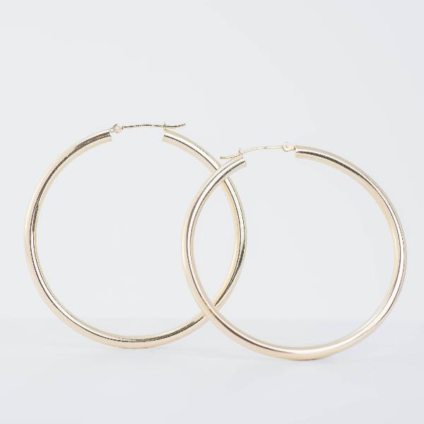 A pair of 14k Yellow Gold Hoop Earrings 3mm exudes sophisticated elegance against a plain, light background. Their large hoops showcase timeless appeal with a smooth, shiny finish and clasp fastenings visible at the tops.