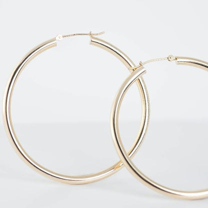 A close-up shot features the 14k Yellow Gold Hoop Earrings 3mm against a light background. These earrings exude sophisticated elegance with their shiny metallic texture and timeless appeal.