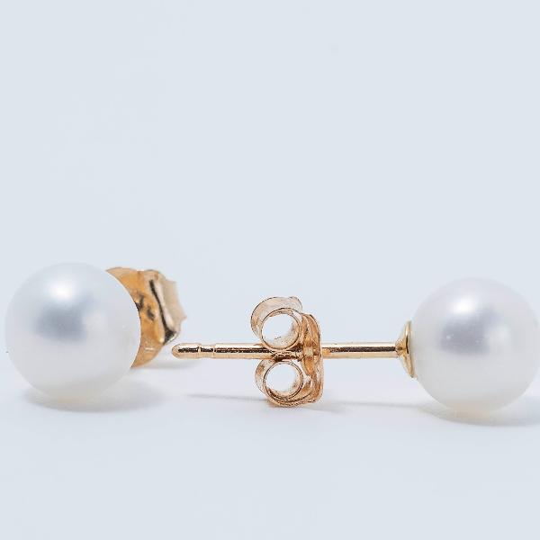 A pair of Youth 5mm Freshwater Pearl Stud Earrings featuring 14K yellow gold posts and butterfly backings displayed against a light gray background. The pearls exhibit a smooth, glossy surface, with one earring facing up and the other positioned lying down.