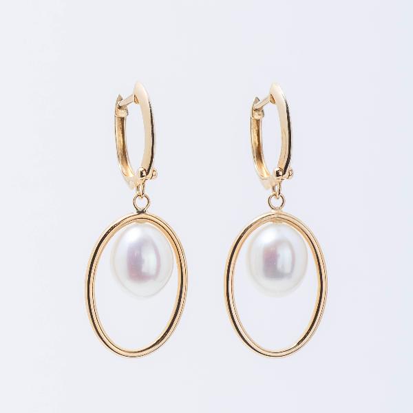 Close-up of the sophisticated 14k Halo White Freshwater Pearl Huggie Hoop Drop Earrings. Each earring features a 14k yellow gold huggie hoop with a hanging round white freshwater pearl, beautifully highlighted against a pale gray background.