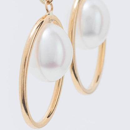 14k Halo White Freshwater Pearl Huggie Hoop Drop Earrings, crafted in yellow gold and showcasing large white freshwater pearls encircled by smooth golden hoops against a light background.