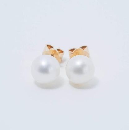 A pair of 14k Classic White 7mm Freshwater Pearl Post Stud Earrings, featuring round, smooth pearls set on a plain white background. The lustrous surface of the pearls emphasizes their timeless simplicity and beauty.