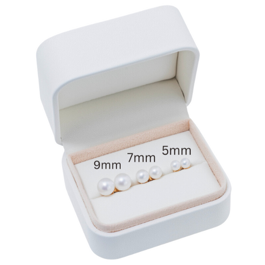 A pristine white jewelry box displays 14k White Freshwater Pearl Stud Earrings Gift Set, featuring three pairs of AAA+ quality pearls in sizes 9mm, 7mm, and 5mm. The exquisite pearls are elegantly presented against a soft cream lining adorned with radiant 14-karat yellow gold accents.