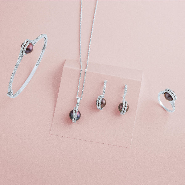 A set of Goddess Jewelry featuring a necklace, earrings, bracelet, and ring with matching designs. Each piece showcases a brown pearl-like stone encircled by a silver band with small diamonds, elegantly displayed on a soft pink background.